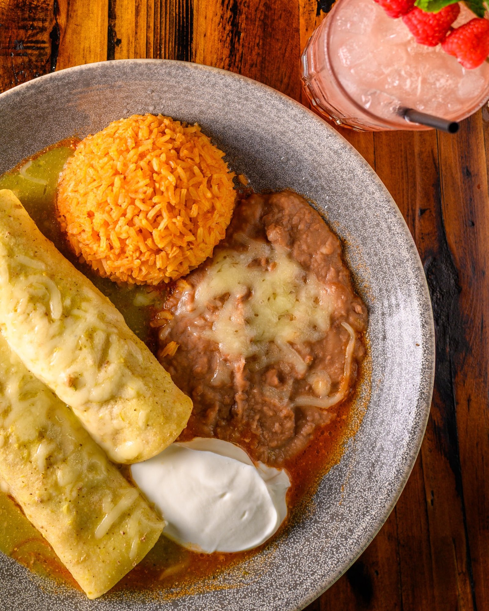 Enchiladas Verdes served with Mexican rice, refried beans, sour cream, and a raspberry drink