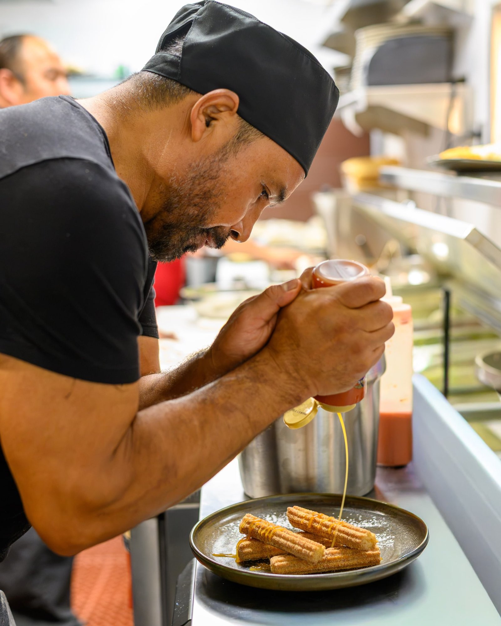 A Don Perico team member finishing a plate of churros with caramel in the kitchen
